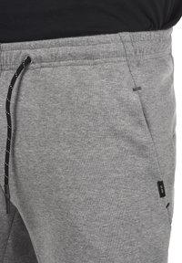 Grå sweatpants med elastisk talje og justerbar sort snor. Har en sidelomme og et lille logo-tag på siden.