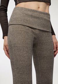 Szare legginsy z filcu z szerokim, złożonym paskiem w talii i gładką fakturą. Zbliżenie podkreśla szczegóły materiału i zwężający się fason.