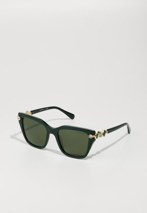 Dunkelgrüne Sonnenbrille mit einer auffälligen Katzenaugenform. Goldene Hardware mit dekorativen Akzenten und einer strukturierten Oberfläche an den Bügeln.