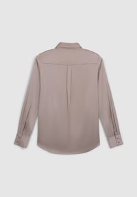 Chemise à manches longues de couleur taupe clair, fabriquée en tissu lisse et brillant. Elle présente un col classique, des poignets boutonnés, et un pli central au dos.
