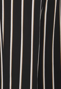 Zbliżenie czarnego materiału z pionowymi białymi i beżowymi paskami, ukazujące złożony lub fałdowany fragment.