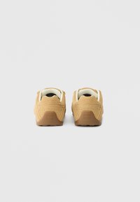 Brown suede sneakers with padded white collars and textured brown rubber soles, featuring small perforations and a logo on the back.