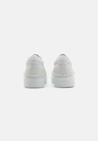 Weiße Sneakers mit glatter Oberfläche, die ein band mit Perlenakzenten um die Zwischensohle und eine robuste Gummisohle aufweisen.