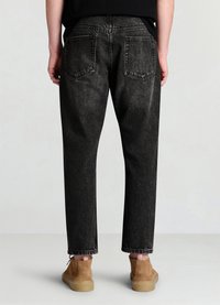 Pantalon en denim noir à coupe large, doté de poches arrière, d'une texture légèrement délavée et d'ourlets cousus, associé à des chaussures marron.