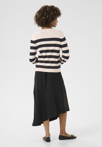 Striped lightweight sweater in beige and black, with a relaxed fit. Paired with a flowing black asymmetric skirt and black flat shoes.
