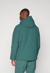 Teal vandtæt jakke med hætte, der har en afslappet pasform og glat tekstur. Inkluderer rygkotelet detaljer og minimale syninger.