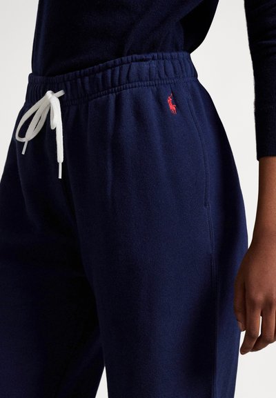 Granatowe spodnie dresowe z elastyczną talią i białym sznurkiem, z małym czerwonym logo na lewej udzie oraz miękką, szczotkowaną teksturą.