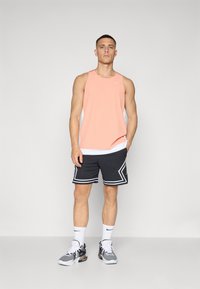 Ferskenfarget treningstop med hvite mesh-sider, kombinert med svarte shorts med hvite striper og perforert tekstur. Grå sneakers.