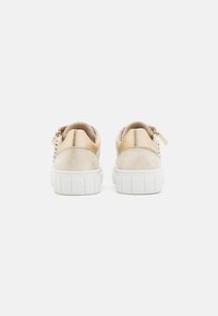 Vista posteriore di sneaker casual caratterizzate da camoscio beige e dettagli metallici, una suola bianca strutturata e una chiusura con zip sul tallone.