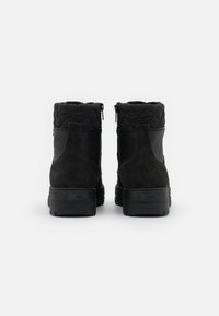 Botines negros hasta el tobillo con parte superior de tejido acolchado, parte trasera de ante y suela de goma. Cuenta con cremalleras laterales y una lengüeta para facilitaar su uso.