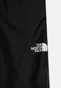 Casaco preto feito de um tecido leve, apresentando uma textura sutil e um logotipo branco proeminente da "The North Face" na parte inferior.
