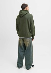 Olivgrüner Kapuzenpullover mit gerippten Bündchen, kombiniert mit locker sitzenden, ausgewaschenen blauen Jeanshosen, die einen leichten Farbverlauf und zwei Hintertaschen aufweisen.