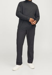 Dunkelgrauer Rollkragenpullover, lockere Passform, kombiniert mit dunkler Hose und weißen Sneakers. Der Stoff wirkt weich mit subtiler Textur.