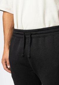 Zwarte joggingbroek met een elastische tailleband, voorzien van een trekkoord en een zachte textuur. De zijaanzicht toont het aansluitende ontwerp en het comfortabele pasvorm.