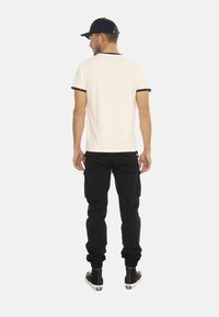 Chemise blanche à manches courtes avec des bordures bleu marine, pantalon cargo noir et bottines noires, vu de dos. Design simple sans motifs.