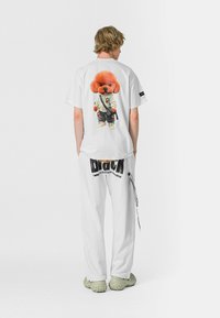 Camiseta de algodón blanca con un colorido perro de dibujos animados en la parte de atrás, llevada con pantalones de chándal blancos adornados con texto negro y una cremallera.