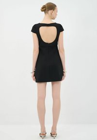 Vestido mini negro con mangas cortas, que presenta un gran corte en la espalda y cierre de cremallera. Tejido suave con acentos de diseño mínimos.