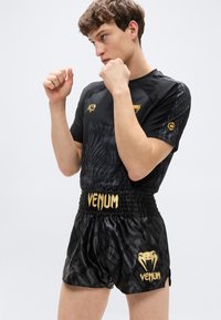 Μαύρο αθλητικό μπλουζάκι με υφή και χρυσές λεπτομέρειες, σε συνδυασμό με μαύρο σορτς με γυαλιστερό φινίρισμα και χρυσλό λογότυπο "Venum".