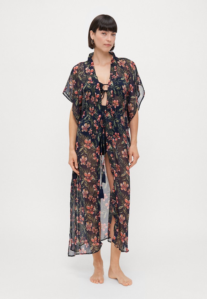 Gjennomsiktig svart kimono med blomstermønster, korte ermer, åpen front, knytefeste og splitt i sidene. Dekorative duskene på knytningene.