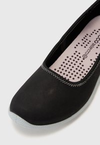Scarpa piatta nera con punta arrotondata, suola grigia strutturata e soletta imbottita rosa con motivo a pois neri. Dettagli cuciti lungo il bordo.