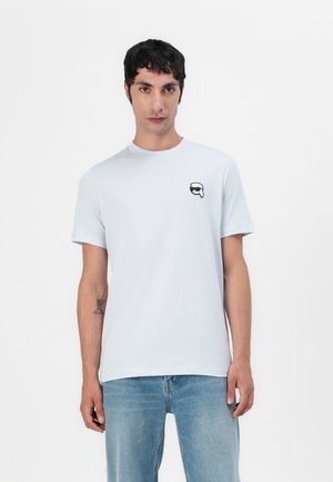 T-shirt di cotone azzurro chiaro con colletto a giro, maniche corte e una piccola grafica nera sulla parte sinistra del petto. Tessuto morbido, vestibilità casual.