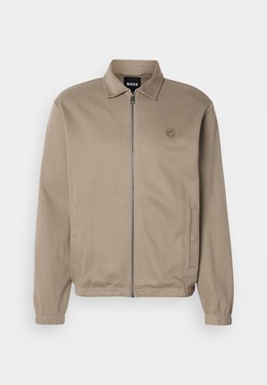 Beige Zip-Jacke mit Kragen, elastischen Bündchen, Seitentaschen und einem tonalen Logo auf der linken Brust. Glattes Material mit einem lässigen Design.