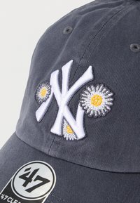 Σκούρο γκρι καπέλο μπέιζμπολ με λευκό κεντημένο λογότυπο "NY" και κίτρινα λουλουδάτα διακοσμητικά. Διαθέτει κυρτή γείσο και ετικέτα αυτοκόλλητο στο μπροστινό μέρος.