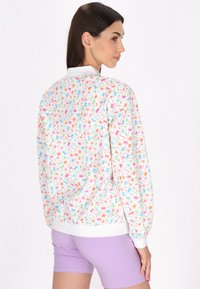 Multifarvet bomberjakke med hvid bund, der har blomsterdesign i pink, orange, grøn og blå; elastiske manchetter og kant.