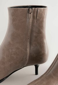 Bottines marron en matériau synthétique texturé, dotées d'une fermeture éclair sur le côté et d'un talon élancé. Fini lisse avec un subtil détail de couture.