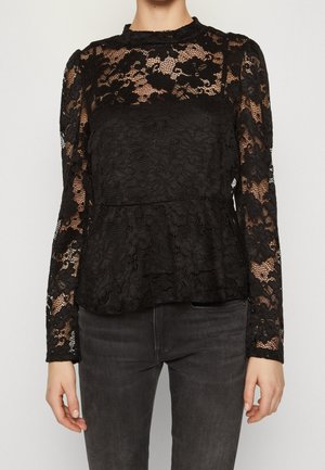 Zwarte kanten blouse met lange mouwen, bloemenpatroon, hoge ronde hals en peplum taille, gedragen met donkergrijze spijkerbroek.