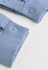 Blauer Baumwollstoff mit gerippter Textur. Verfügt über Knopfdetails in derselben Farbnuance und umgeschlagenen Kanten, die eine saubere Verarbeitung zeigen.