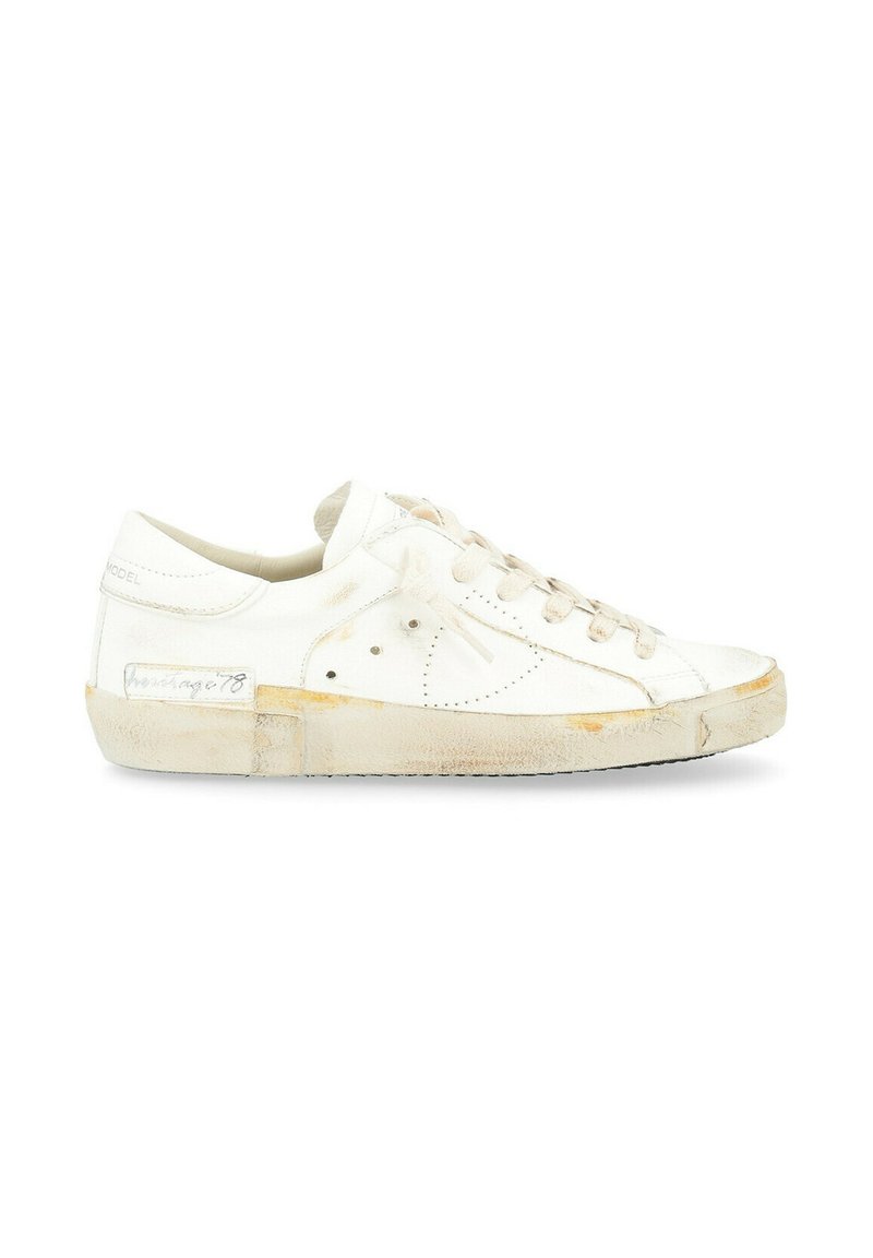 Sneaker in pelle bianca con profilo basso, punta arrotondata, design perforato, lacci color crema e suola in gomma leggermente usurata e ingiallita.