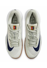 White athletic shoes with a textured upper, navy swoosh, prominent lacing, and a light brown rubber sole. Features a logo and model name.