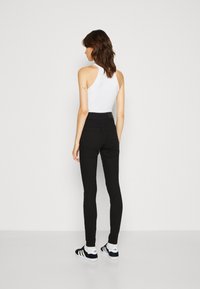 Jeans skinny negros de cintura alta con una textura suave y una silueta ajustada. Llevados con una blusa blanca sin mangas y zapatillas negras.