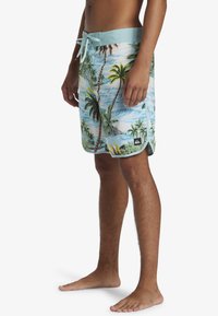 Board shorts with a light blue waistband and tropical palm tree print in green and brown on a white background. Quick-dry fabric.