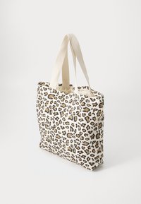 Canvas tote bag with a white background and brown leopard print. Features two fabric straps for carrying. Rectangular shape with open top.