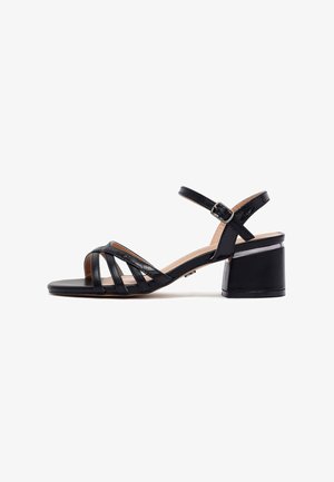 Black leather heeled sandals with an open toe design, featuring crisscross straps and an adjustable ankle buckle, on a block heel.
