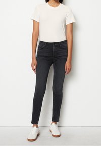 Valkoinen ribattu t-paita yhdistettynä tummanharmaisiin skinny-farkkuihin, joissa on klassinen viisi-taskuinen muotoilu. Käytössä valkoiset lenkkarit.