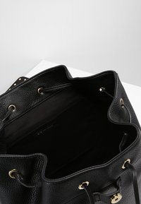 Bolso de mano tipo cubo de cuero negro con una superficie texturizada, herrajes dorados y un interior de tejido suave. El interior cuenta con una etiqueta de logotipo y un cierre con cordón.