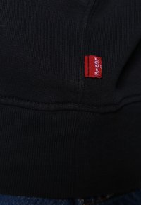 Black ribbed fabric, featuring a red Levi's logo label stitched on the hem. The texture is smooth and slightly stretchy.
