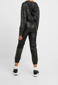 Svart croppad hoodie med en grå strukturerad mönster, i kombination med svarta faux läder joggers med elastiska manschetter och sidofickor. Vita sneakers.