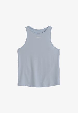 Jeune femme en tenue de sport tenant une bouteille d'eau en métal, debout contre un mur clair uni, regardant sur le côté.