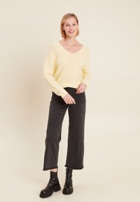 Hellgelbes, flauschiges Strickpullover mit V-Ausschnitt. Kombiniert mit hochgeschnittenen, schwarzen, eng anliegenden Jeans und klobigen schwarzen Stiefeletten.
