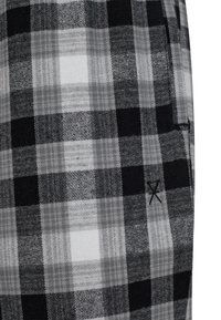 Black and white plaid fabric featuring various check sizes and textures, with a small stitched accent in black.