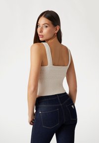 Beige gebreid cropped top met brede geribbelde schouderbanden en een gestructureerde taille. In combinatie met donkerblauwe high-waisted jeans met achterzakken.