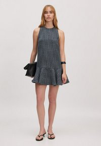 Ärmelloses schwarzes und weißes gemustertes Kleid mit einem ausgestellten Saum, aus strukturiertem Stoff. Kombiniert mit einer schwarzen Clutch-Tasche und minimalistischen Sandalen.