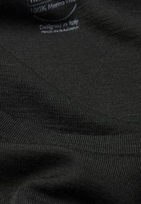 Schwarzer gestrickter Stoff mit einer sanften Textur, mit einem Etikett, das "100% Merinowolle" angibt, entworfen in Italien. Nahaufnahme zeigt feine Nähte.