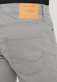 Harmaat farkut, joissa on nahkainen brändilogo kohokirjoituksella, hienovaraiset takataskun ompeluaukot ja tavalliset metalliosat.