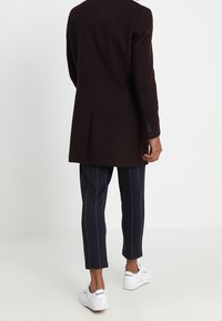 Abrigo burdeos oscuro con un diseño ajustado, que presenta una abertura simple en la parte posterior. Combinado con pantalones azul marino de rayas y zapatillas blancas.