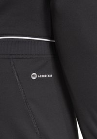 Zwarte sportstof met een strak ontwerp, voorzien van een wit logo "AEROREADY" en een witte accentlijn langs de tailleband.